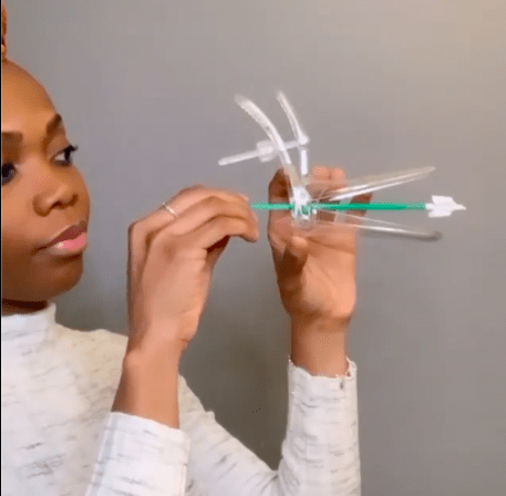 Dr Aziza Sesay is holding up a speculum and cervical screening brush