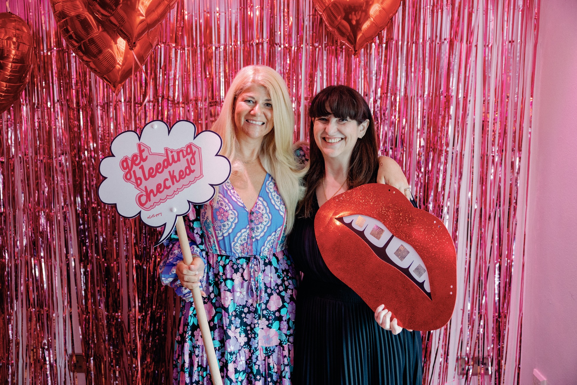 Two people with signs smiling with a pink backdrop